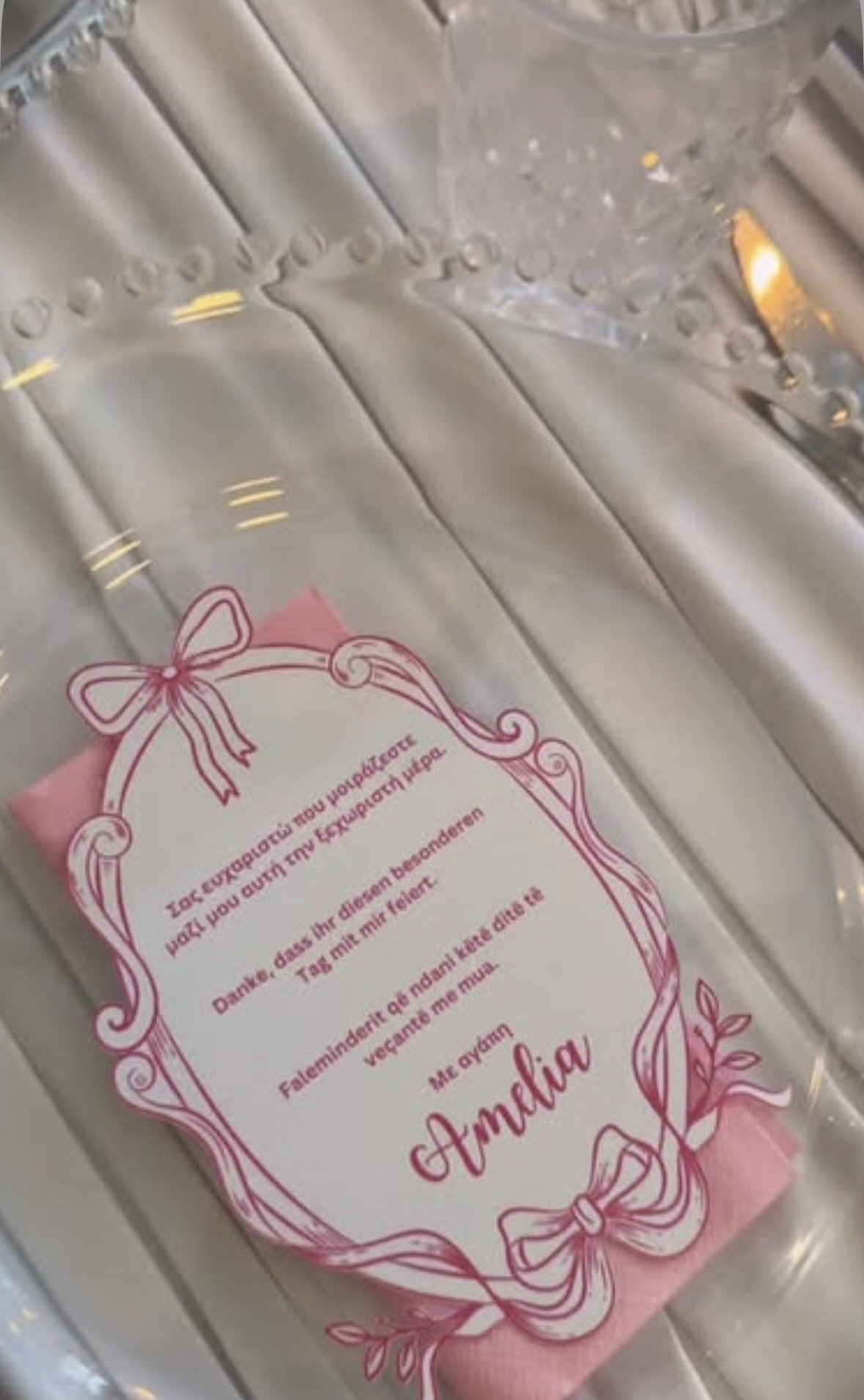 Nahaufnahme einer Platzkarte mit rosa Rahmen und Schleife auf einer rosa Serviette, Dank in drei Sprachen