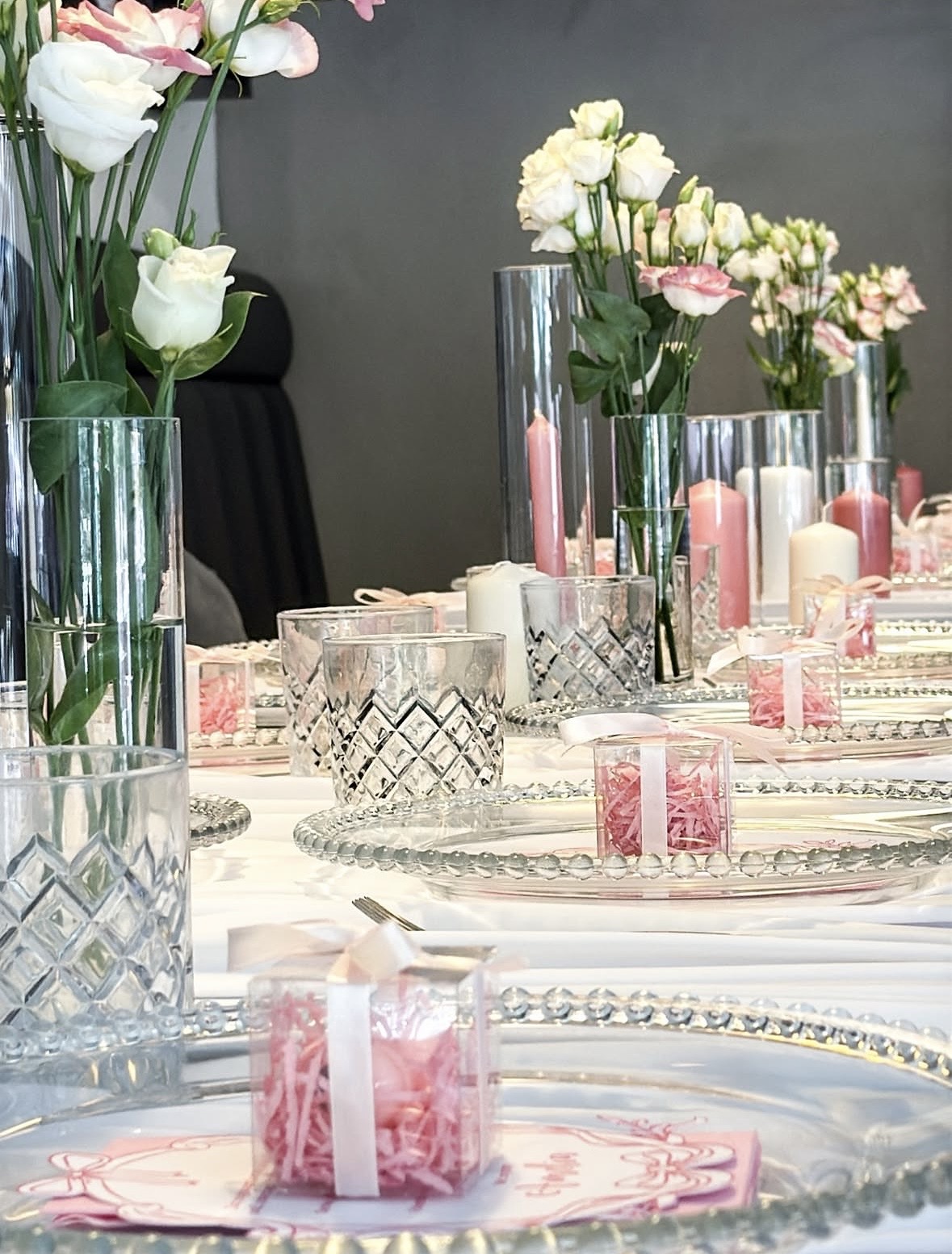 Tauftafel mit Kristallbechern, Geschenkboxen mit rosa Füllung, Kerzen in Glaszylindern und weißen Lisianthus