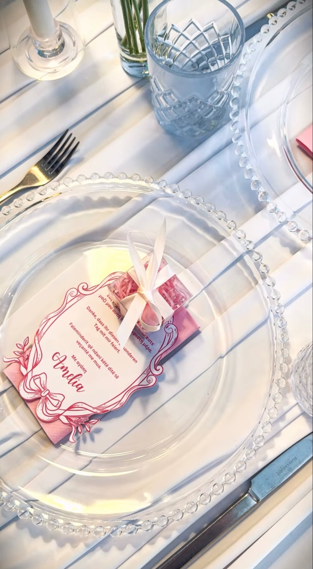 Platzteller mit Perlenrand von oben, darauf eine Platzkarte mit gezeichnetem rosa Rahmen und Schleife und eine kleine Geschenkbox